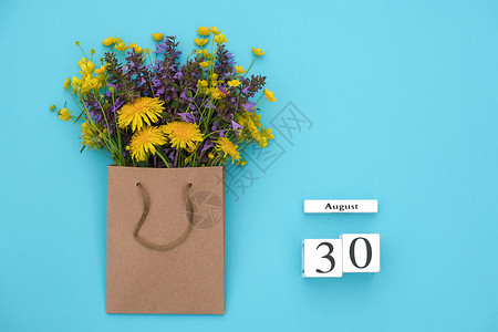 明信片8月30日Wooden立方体日历8月30蓝背景的手工艺品包中花朵多彩生鲜蓝色背景的GreetingcardFlatLay概图片