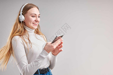 头发常设年轻女孩聆听音乐流内容于观看视频享受聊天与朋友使用智能耳机对面做手势表情的交谈坐在浅灰色背景上的耳机随意图片