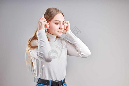 脸复制清楚的年轻女孩聆听音乐流内容于观看视频享受聊天与朋友使用智能耳机对面做手势表情的交谈坐在浅灰色背景上的耳机图片