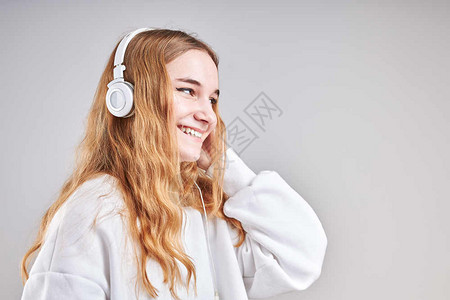 年轻女孩聆听音乐流内容于观看视频享受聊天与朋友使用智能耳机对面做手势表情的交谈坐在浅灰色背景上的耳机面孔随意的女图片
