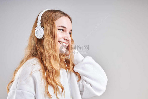 年轻女孩聆听音乐流内容于观看视频享受聊天与朋友使用智能耳机对面做手势表情的交谈坐在浅灰色背景上的耳机面孔随意的女图片