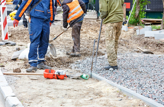 劳工道路施人用铲子在行道上准备一个沙质地基并用水泥路边的瓦砾覆盖该地一个建筑工小组正在筹备铺筑人行道的奠基在一天晴朗的时空复制间图片