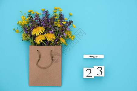 展示布局8月23日Wooden立方体日历和蓝背景的手工艺品包中富彩的生鲜花蓝色背景的GreetingcardFlatLay概念喜图片