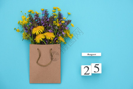 有创造力的明信片Wooden立方体8月25日历和蓝背景手工艺品包中富彩的生鲜花蓝色背景的GreetingcardFlatLay概图片