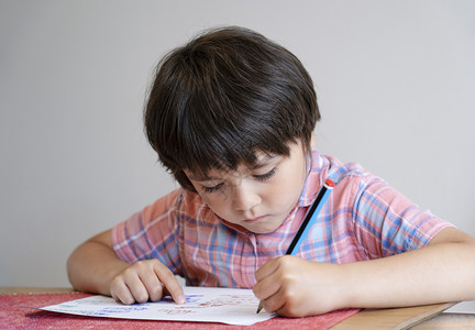 笔记本在家工作坐桌边做功课的男孩子肖像快乐儿童拿着铅笔写作一个男孩在桌子上用白皮书画小学和家庭校概念以及一名男孩在餐桌上用白纸画图片