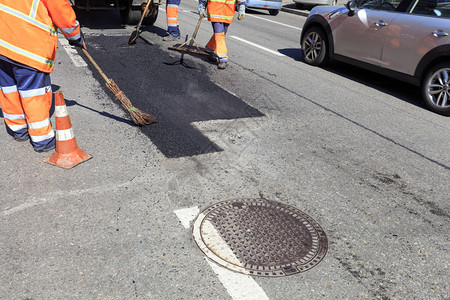 沙井附近的道路工人作组用新鲜的热沥青修复部分道路并使用各种手动工具铲子水平仪扫帚将其抹平更新黑色的建造图片