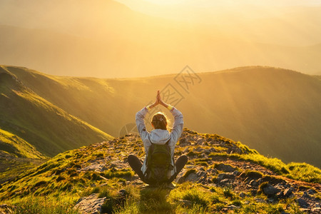 放松带着背包坐在山峰上的年轻女人和在夏季日落时雾中的美丽山上风景与运动女孩绿林山丘天空太阳光和旅游瑜伽比利茨基瓜拉纳皮图片