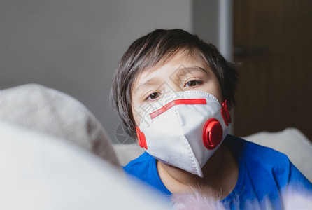 疲劳的身戴医疗面罩在下午25时保护他带着悲伤脸的孤独儿童男孩呆在家里以接受冠状流感爆发和疾病的保护在医院里孩子面对紧贴近身的脸看图片