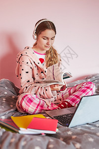 在线的大流行学生在线习远程观察课听教授在家中用笔记本电脑耳机书本手册对女孩进行隔离时通过视频电话与在家的同学交谈并坐在床上数字的图片