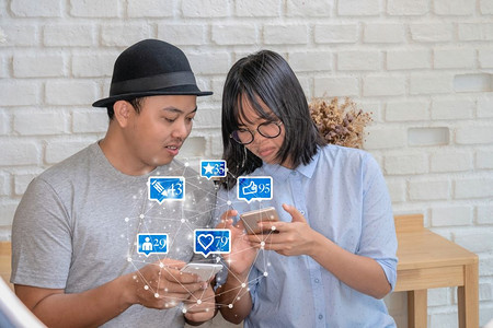 朋友最喜欢的营销在现代咖啡店或工作场所使用智能手机的亚洲青年夫妇用于社交网路媒体包括类似爱评论人和fovotorite图标社交网图片