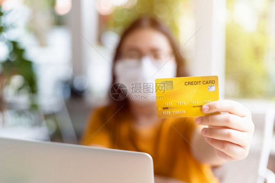 身着保护面罩的女商人自由职业者穿戴保护面罩的业余休闲女摘要模糊重点为显示持有信用卡在咖啡店笔记本电脑工作如背景在家工作亚洲安全图片