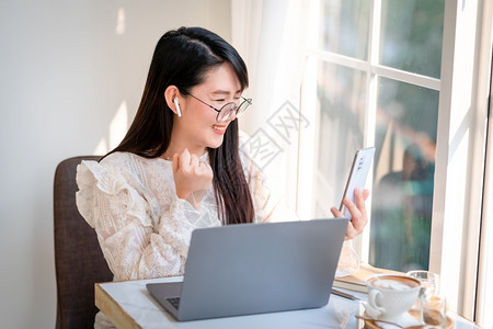 专业的成人商女在智能手机上写信息并举行咖啡杯茶在咖啡馆商务生活方式用笔记本电脑工作的闲高兴极了图片