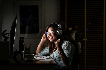 咖啡聪明的机构亚洲女商人通过耳机和智能手收听音乐的肖像在工作场所晚些时候在桌面上欢庆行动努力工作为时过晚的概念图片