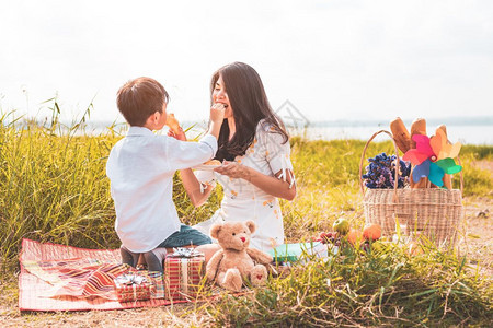 孩子厨师垫母亲和儿子一起在母亲节庆祝并欣赏夏季人与生活方式的概念他妈在草地上吃零食时在野餐中互相吃着小点心图片