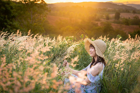 时尚女孩戴帽子穿白色衣服坐在草地中间花朵美丽的白在太阳下定时间在山上放松和快乐的心情年轻泰国图片