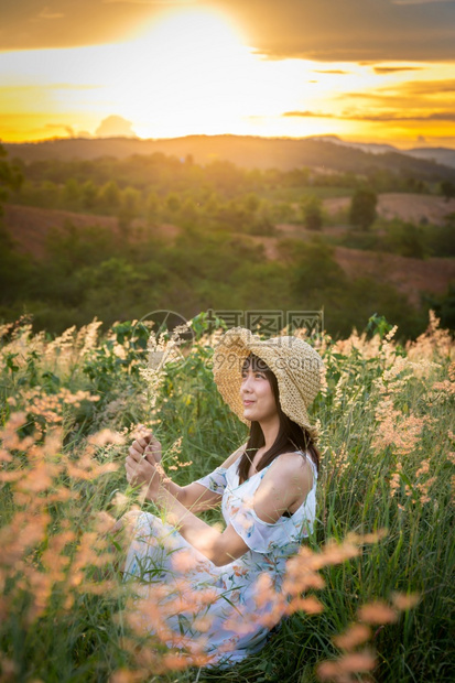 场地女孩戴帽子穿白色衣服坐在草地中间花朵美丽的白在太阳下定时间在山上放松和快乐的心情模型户外图片