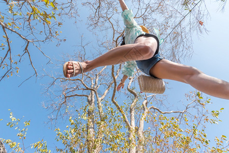 低的相机角度观察感女短牛仔裤中空跳跃跨过摄像头在森林下拍摄概念旅行积极生活方式克服障碍方面树上和天空高架的概念旅行妇女跳跃或越森图片