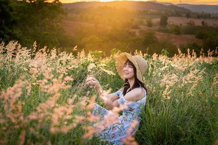 裙子空气人们女孩戴帽子穿白色衣服坐在草地中间花朵美丽的白在太阳下定时间在山上放松和快乐的心情图片