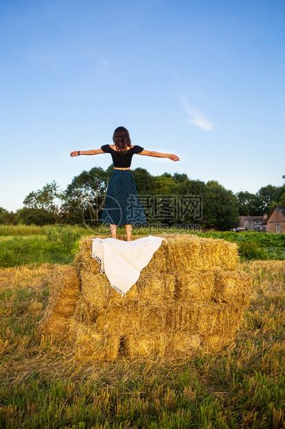干草年轻美女站在一大堆稻草捆上自由风落日年轻美女站在一大堆稻草捆上自由落日夏天肩膀图片