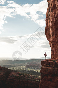 户外垂直的成功一个人站在悬崖边上的远景垂直拍摄在晴朗的天空下被丘陵和山脉环绕图片
