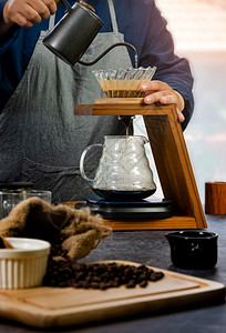 咖啡因锥体在地面咖啡纸张过滤器和放在木制持者下面的玻璃容器中收集的手工滴水在地面咖啡上浇水的杯师图片