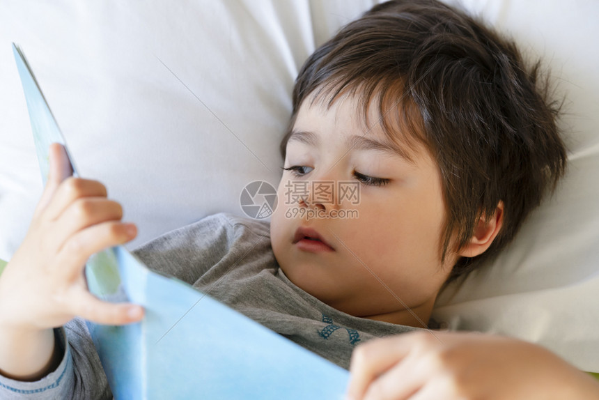 说谎男白色的一个快乐孩子躺在床上阅读一本书快乐的孩子男在睡觉前读他的喜悦故事书睡前的床时间故事概念图片