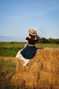 场地农业户外戴草帽的年轻美女看着夕阳孩坐在一大堆草捆上温暖的夏夜戴草帽年轻美女看着夕阳孩坐在一大堆草捆上温暖夏夜图片