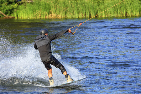 娱乐木板一名滑水运动员沿着河岸高速冲过水一只手拉着缆绳在自己周围形成一团喷雾名滑水运动员沿着绿色的河岸高速冲过水喜悦图片