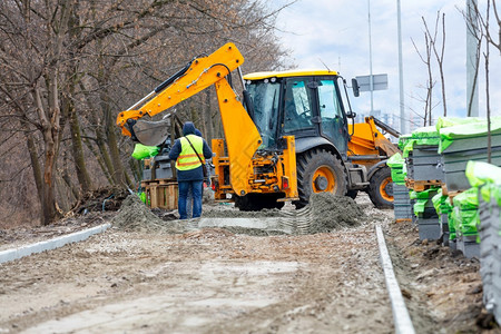 瓦工抑制一个作队使用道路挖掘机将成堆的铺路板卸到边以进行后续铺装民事图片