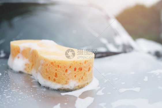 湿的肥皂水气泡洗车用黄色海绵和汽车上洗衣用的肥皂清洗汽车头罩被概念车清洁休假空间用于撰写信息图片