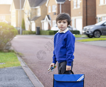 跳线途径无聊的脸拿着塑料玩具和背包等待校车的书小学的无助生在路上独自站边看着带悲伤面的照相机Kid回到学校不开心图片