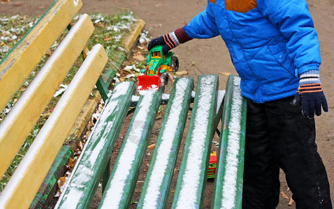 黑暗的建造一个小孩站在木凳附近被雪覆盖的部分图像孩子用玩具挖掘机从长凳上清除积雪椅图片