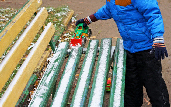 黑暗的建造一个小孩站在木凳附近被雪覆盖的部分图像孩子用玩具挖掘机从长凳上清除积雪椅图片