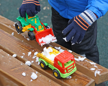 常设季节拖拉机一个小孩站在木凳附近被雪覆盖的部分图像孩子用玩具挖掘机从长凳上清除积雪图片