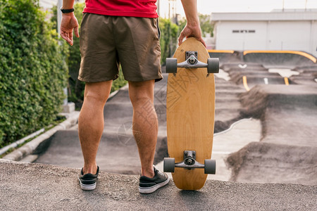 紧闭亚洲男子在滑轮冰公园持有冲浪skate或滑板当时日出间超过泵轨曲线转盘运动健康和锻练时尚等相光模糊点的日出时间极端青少年长板图片