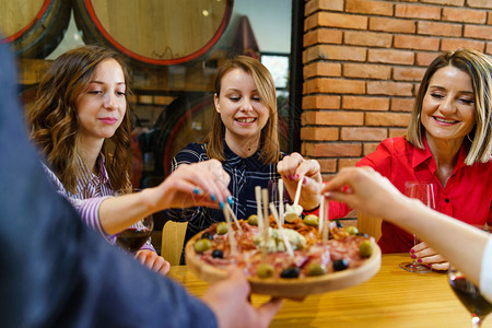 三名女天主教孩坐在桌边拿着红酒杯而不明男子正在家里或餐馆为开胃小吃的朋友提供白天微笑的餐饮享受白种人坐着图片