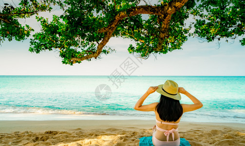海滩穿着粉红泳衣和草帽放松在树下热带沙滩享受节假日暑时装的美女夏日时装感模特儿夏天情调时尚蓝色的图片