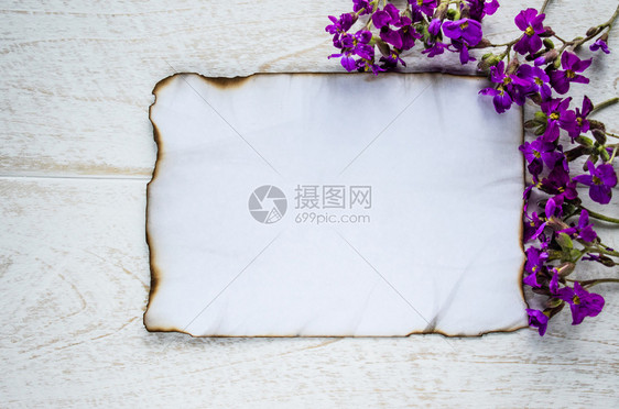 房间笔记本平坦的在白色木板上边缘燃烧着一张白纸紫色的花朵为文字留出了空间图片