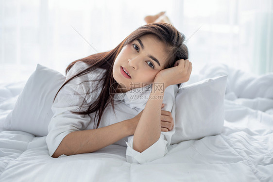 疲劳的睡眠背部亚洲女人美丽的年轻微笑女人坐在白床上睡觉早在卧室里舒展身体在床上醒来后充分休息图片