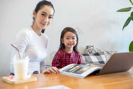 电脑女亚洲母亲正在教女儿阅读一本书并使用笔记本和技术在家庭学校放假期间进行网上学习教育概念和家庭活动教育概念与家庭活动利用笔记及图片