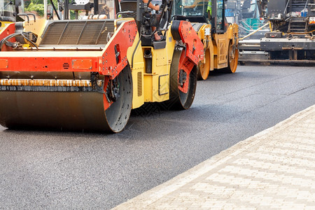 黄色和橙的道路振动压机紧随摊铺后在新的道路施工现场压实新鲜沥青人行道基辅滚筒图片