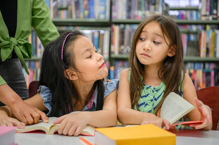两个可爱的女孩互相嫉妒同时在图书馆阅读本而教师则在学校概念主题日托中教授人们的生活方式和教育人与之间的生活方式和教育青年友谊与儿图片