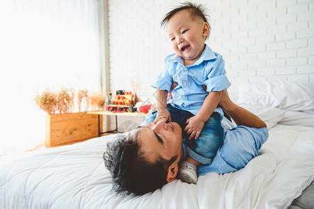 两个亚裔父亲和儿子躺在床上卧室里玩耍孩子在日本爸的身体上快乐休闲时间人们生活方式健康爱隔离Covid19Corana放松他的日本图片