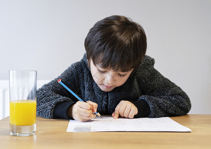 男生可爱的孩用笔写在白皮书上的纸学生在家时做拼写测试在家庭学校概念中生们做了拼写测试a独自的教育背景图片