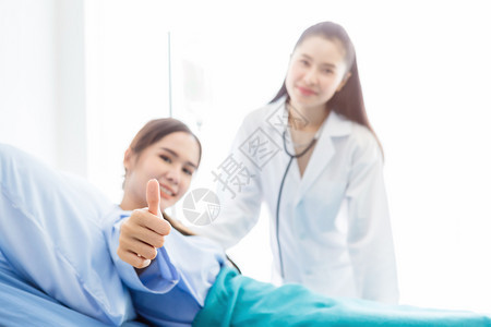 剪贴板护士亚洲年轻女患者躺在床上摘要模糊不清重点节目显示在医院背景的亚洲年轻女医生面前以微笑的脸表露出拇指和笑脸吸引人的图片