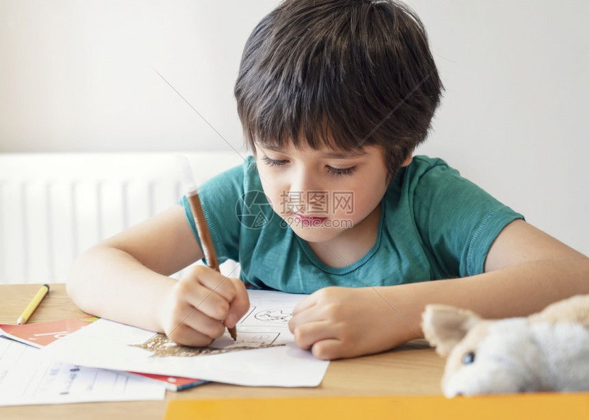 学龄前儿童生坐在桌边做功课的男孩子肖像快乐儿童拿着铅笔写作一个男孩在桌子上用白皮书画小学和家庭校概念以及一名男孩在餐桌上用白纸画图片