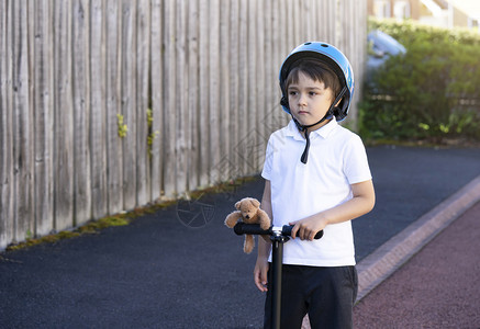 儿童身着安全头盔骑滚车带着泰迪熊站的小孩看深思熟虑为儿童积极休闲和户外运动等活c儿童快速地乐的玩图片