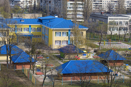 草树木幼儿园亮蓝色屋顶在灰城市高层建筑的背景下被春天阳光照亮幼儿园明的蓝色屋顶在灰城市高层建筑的背景下沙盒图片