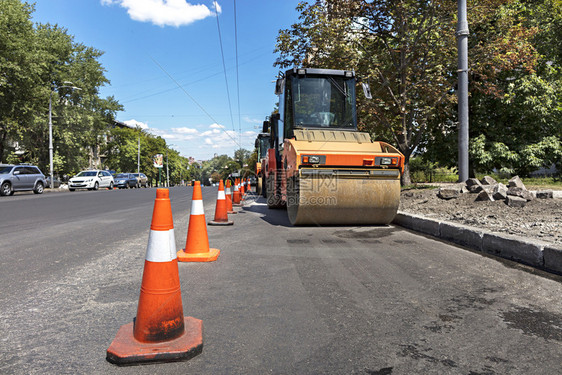 沥青构造车轮橙色公路锥体保护在城市街道上重振动压板的工作场所橙色公路锥体保护沿城市街道边缘的重型轮式紧压机以及图片