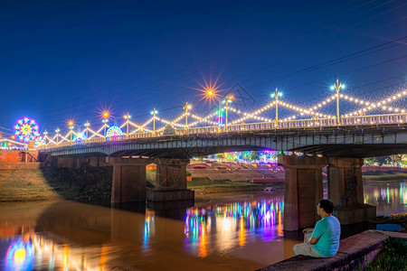 这名年轻人在夜里看着南河上美丽的光芒晚上在内川纳里苏大桥NaresuanBridge上在泰国的Phitsanulok举行大节和红图片